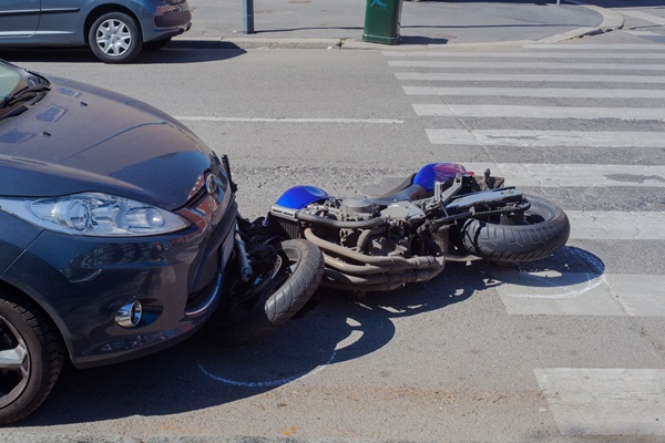 A motorcycle lodged underneath the front end of a blue car following a motorcycle accident.