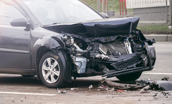 Heavily damaged front end of a black car involved in a serious crash, with debris scattered on the road.